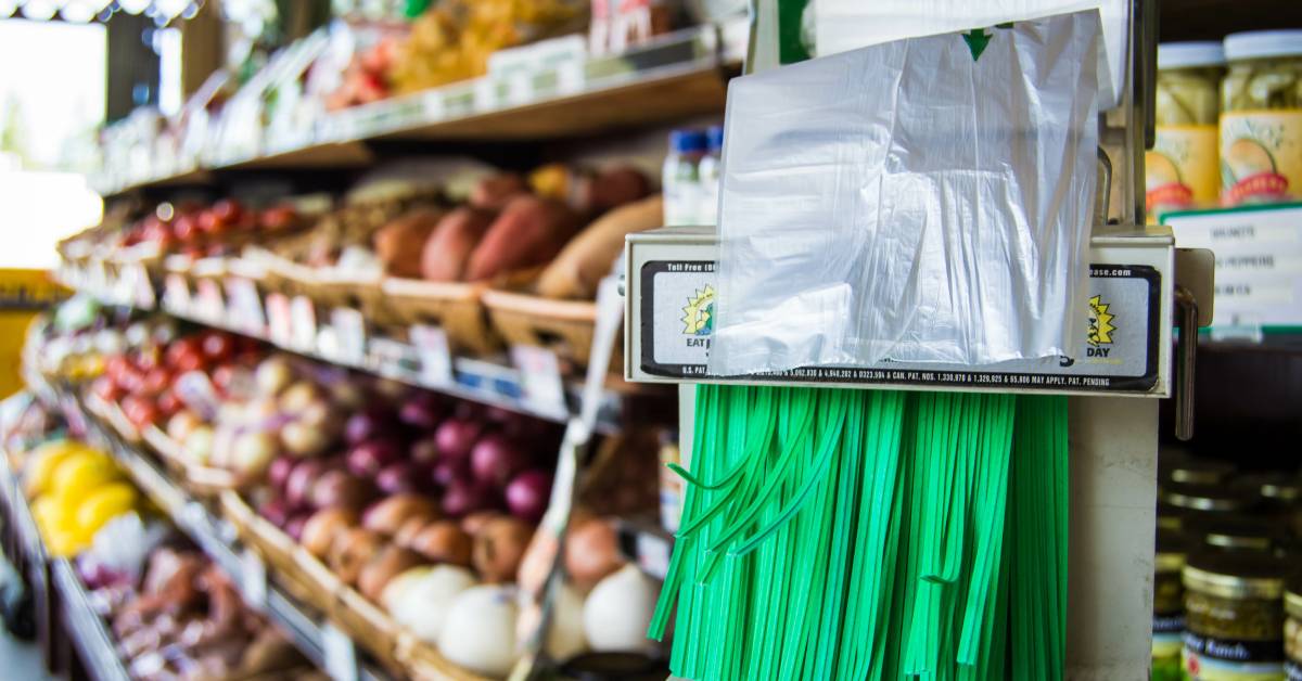 Closeup of several green twist ties in a dispenser in a grocery store with fresh produce displays in the background.