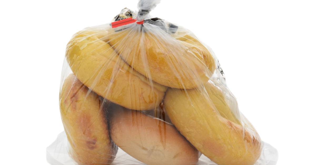 A clear plastic bag is tied at the top with a paper twist tie. Inside the big are five different brown bagels.