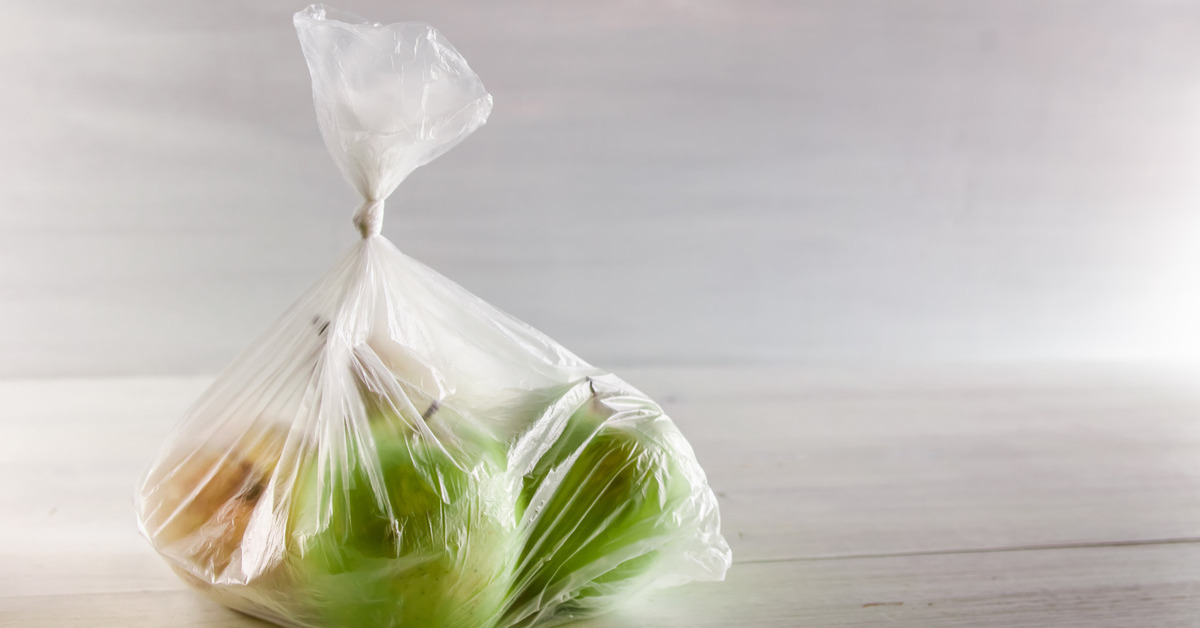 Close-up of a tied plastic produce bag filled with several green apples sitting on top of a light wooden table.