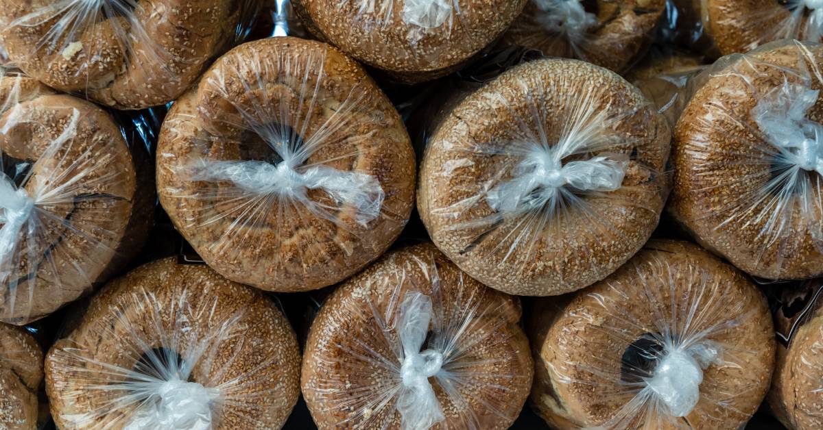 A bunch of plastic bags full of bagels are all stacked on top of each other with the tied end facing outwards.