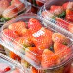 Closeup of several stacks of plastic produce packaging containers filled with strawberries with price labels.